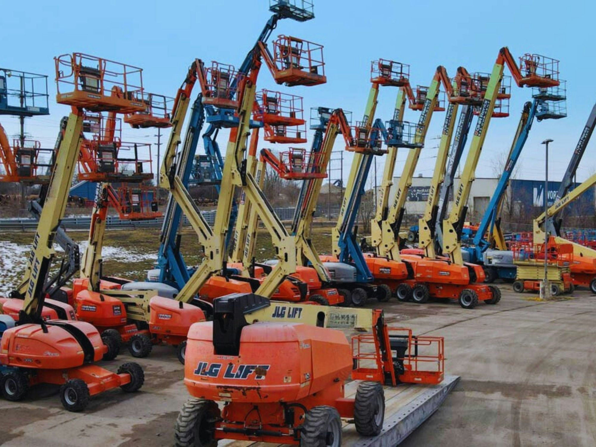 Boom lifts and scissor lifts lined up in a rental yard in winter